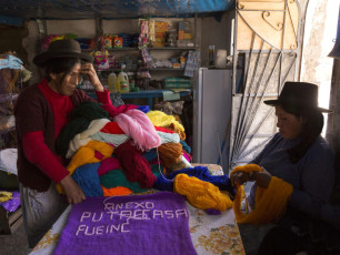 A woman in her store with a family member. She is making a weaving for the memory of her hometown, Putaccasa, where she was raped during the years of violence. The Shining Path burned down Putaccasa twice, in 1984 and in 1992. Sacsamarca, Ayacucho Region, 2014